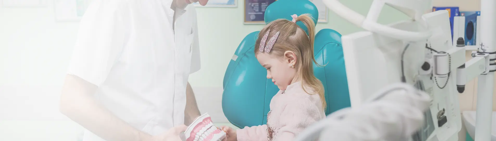 A child sitting in a dental chair while the dentist shows a tooth model.