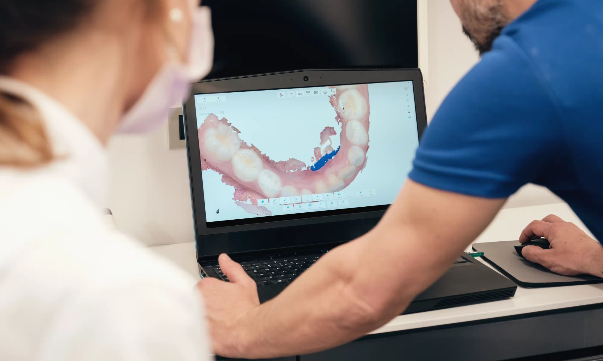 Stomatolog i pacijent gledaju 3D digitalni model zuba prikazan na ekranu laptopa